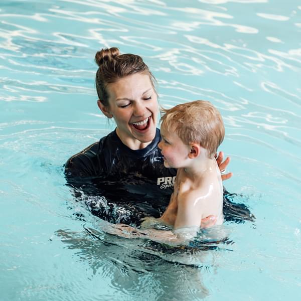 Smiling, happy PRO Club Aquatics instructor teach a child to swim