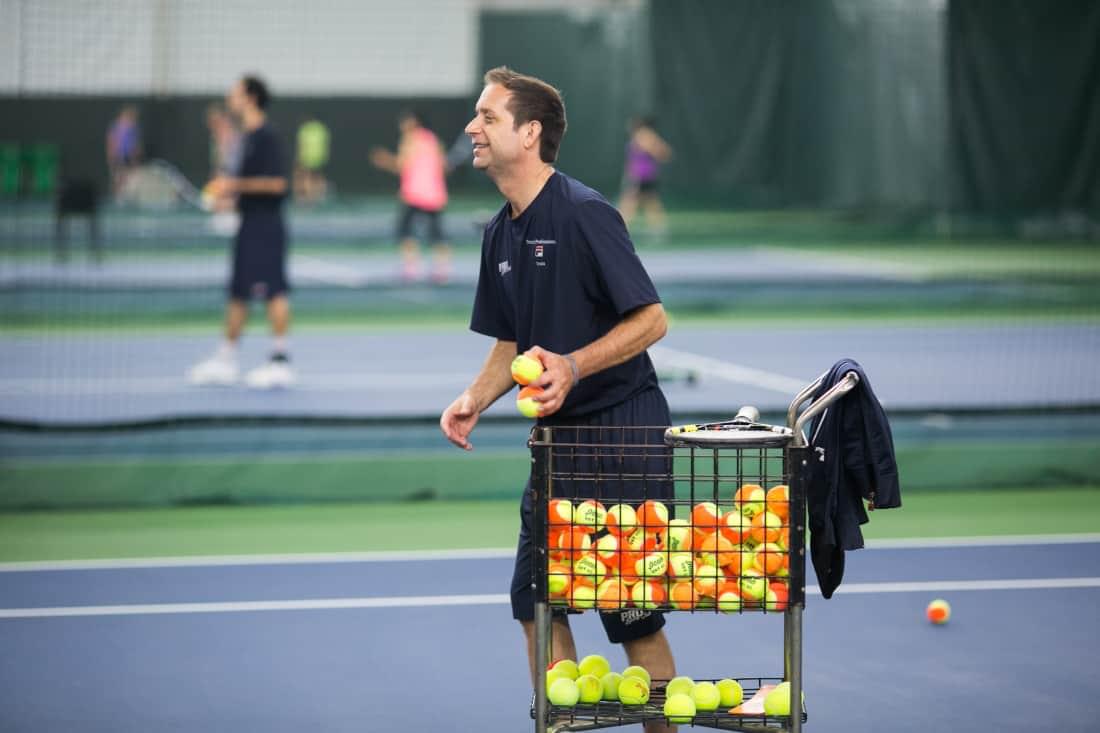 Smiling man serving up tennis balls to a Tennis member at PRO Club
