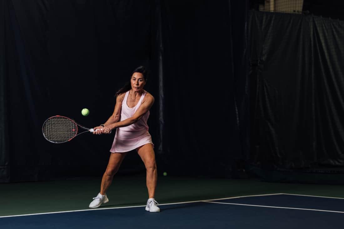 Woman in pink tennis outfit returning a serve on one of PRO Club's tennis courts